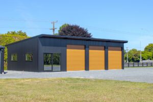 Custom pole shed with three large wooden garage doors, large windows, and a sleek black and wood exterior, set against a grassy field.